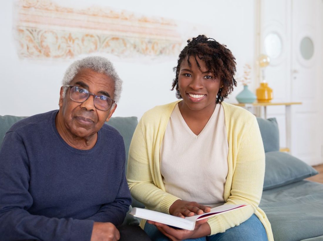 A caregiver reading with an older man on the couch